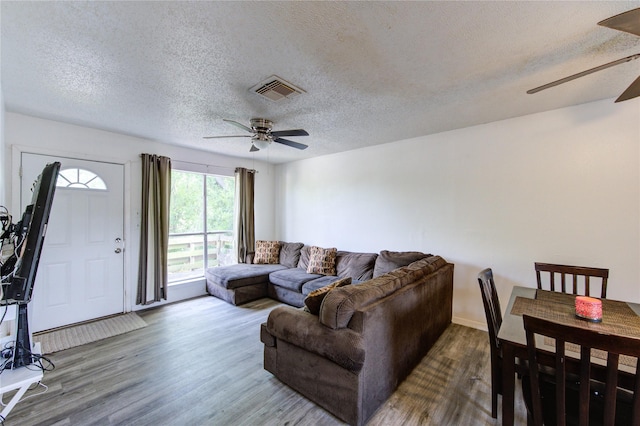 living area featuring visible vents, a ceiling fan, a textured ceiling, and wood finished floors