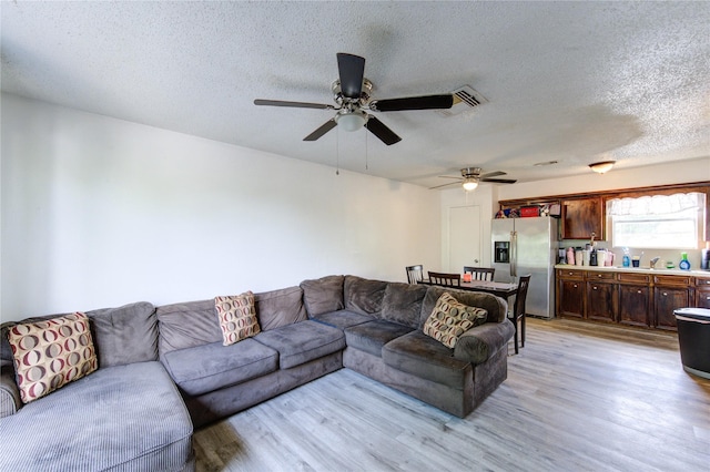 living room with a textured ceiling, ceiling fan, light wood-style flooring, and visible vents