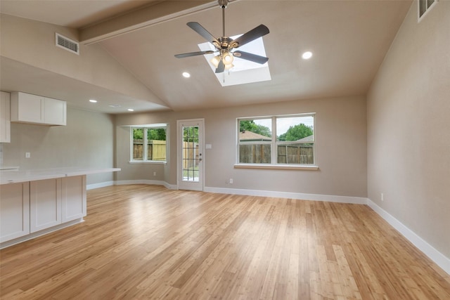 unfurnished living room featuring vaulted ceiling with skylight, a ceiling fan, light wood-style flooring, and visible vents