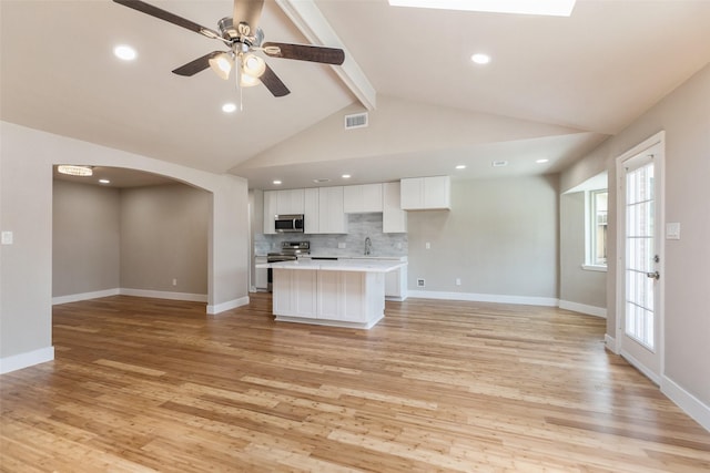 kitchen with open floor plan, light countertops, white cabinets, arched walkways, and appliances with stainless steel finishes