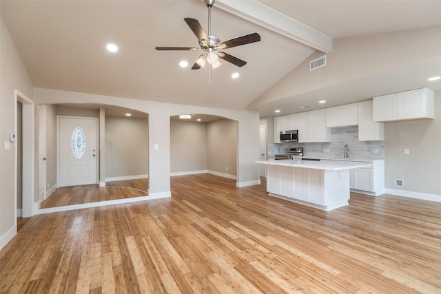 kitchen featuring visible vents, a sink, a center island, arched walkways, and appliances with stainless steel finishes