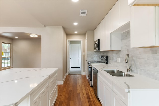 kitchen featuring a sink, arched walkways, stainless steel appliances, baseboards, and decorative backsplash