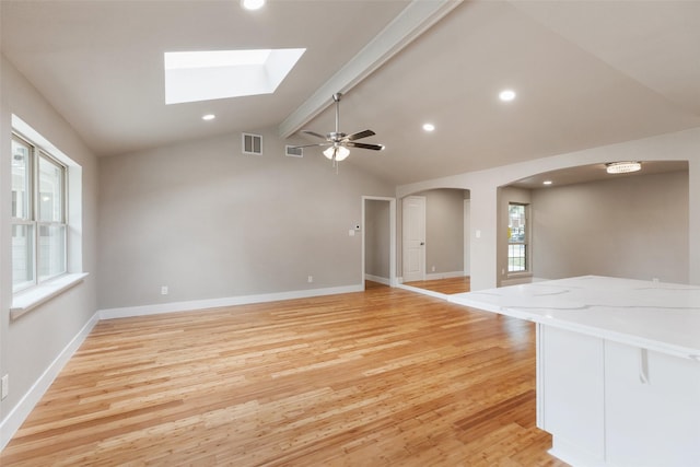 unfurnished living room with vaulted ceiling with skylight, ceiling fan, visible vents, arched walkways, and light wood-type flooring