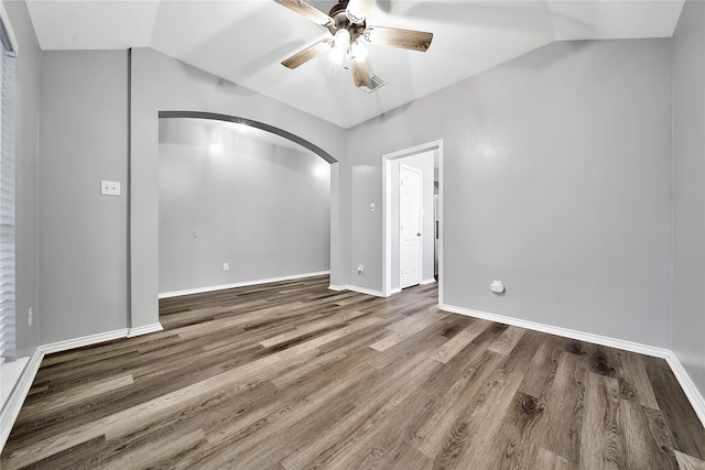 spare room featuring wood finished floors, baseboards, ceiling fan, arched walkways, and vaulted ceiling