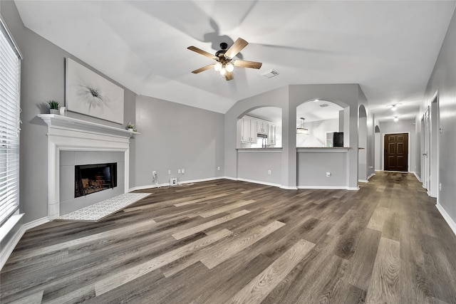unfurnished living room with dark wood-style flooring, ceiling fan, a fireplace, a wealth of natural light, and visible vents