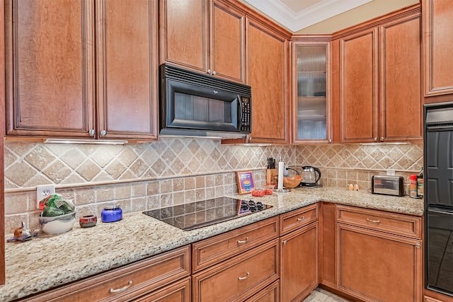 kitchen featuring glass insert cabinets, ornamental molding, light stone countertops, and black appliances