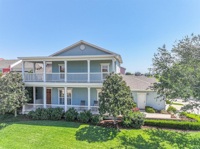 greek revival inspired property featuring covered porch, stucco siding, a front lawn, and a balcony