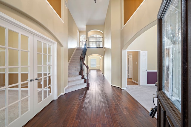foyer entrance with arched walkways, a high ceiling, dark wood-style floors, and french doors