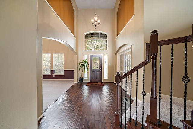 foyer featuring a towering ceiling, stairway, baseboards, wood-type flooring, and a chandelier