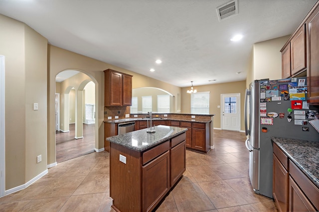 kitchen featuring visible vents, arched walkways, dark stone counters, and a peninsula