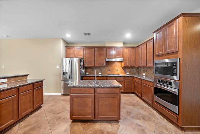 kitchen with visible vents, under cabinet range hood, dark stone countertops, appliances with stainless steel finishes, and backsplash