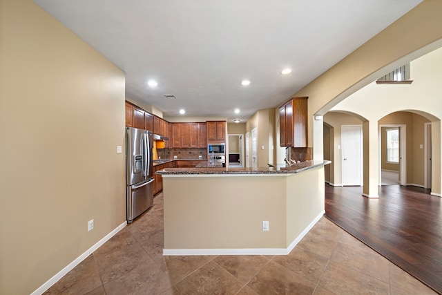 kitchen featuring appliances with stainless steel finishes, arched walkways, dark stone counters, recessed lighting, and a peninsula