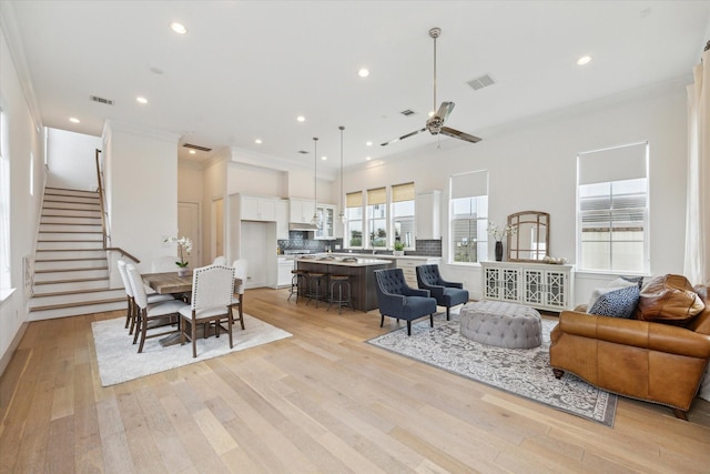 living room with crown molding, ceiling fan, light wood-style floors, stairs, and visible vents