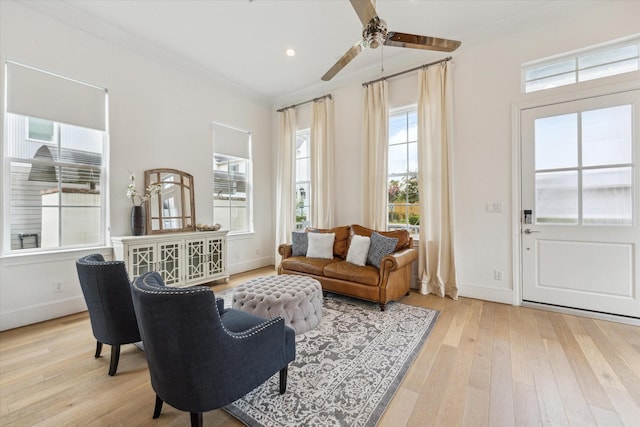 living area featuring wood-type flooring, a ceiling fan, baseboards, and ornamental molding