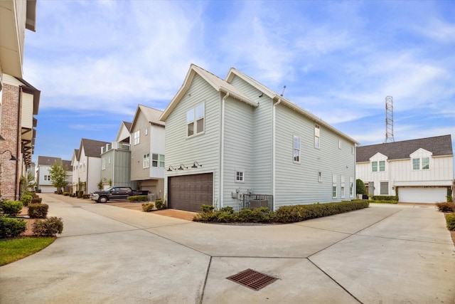 view of property exterior featuring a residential view, an attached garage, central AC, and driveway