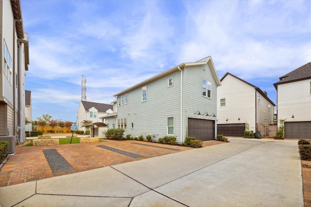 view of side of property with a garage, a residential view, concrete driveway, and cooling unit