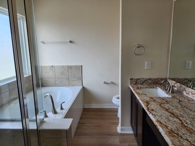 bathroom with a garden tub, wood finished floors, baseboards, vanity, and toilet