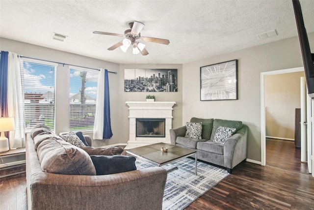 living room featuring visible vents, ceiling fan, a textured ceiling, a tiled fireplace, and dark wood finished floors