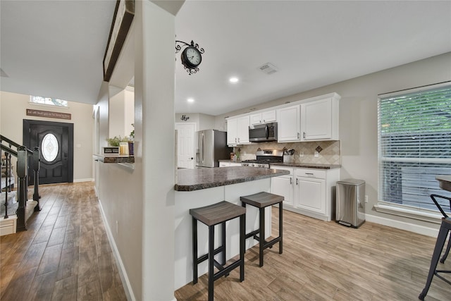 kitchen featuring a breakfast bar area, visible vents, dark countertops, baseboards, and stainless steel appliances