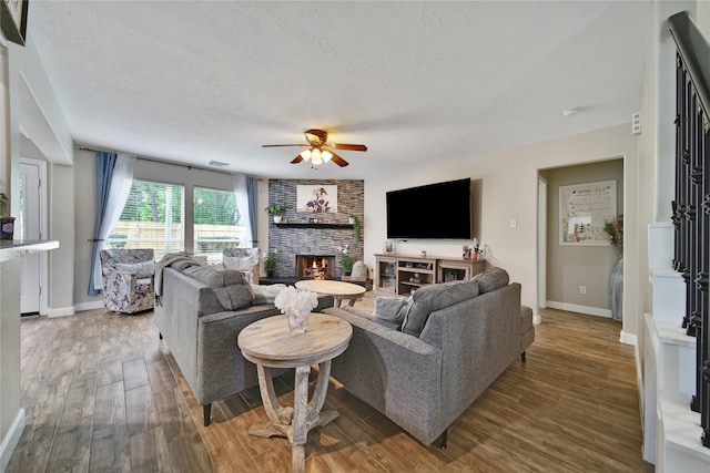 living room with ceiling fan, a textured ceiling, a fireplace, wood finished floors, and baseboards
