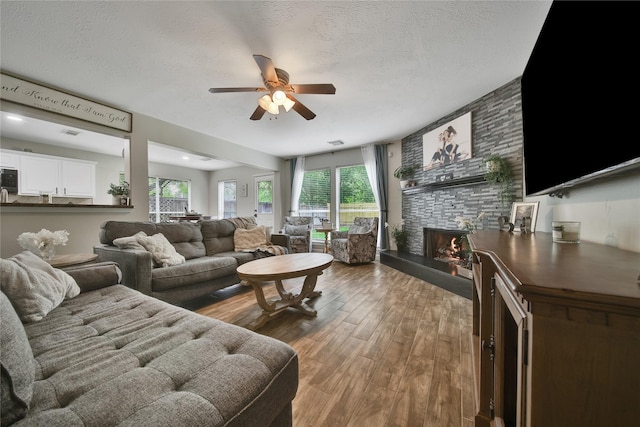 living area featuring visible vents, wood finished floors, a fireplace, ceiling fan, and a textured ceiling