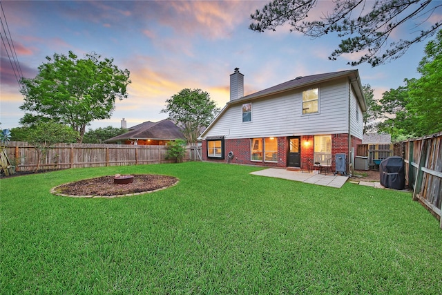 back of property featuring brick siding, a fenced backyard, a chimney, a patio, and a yard