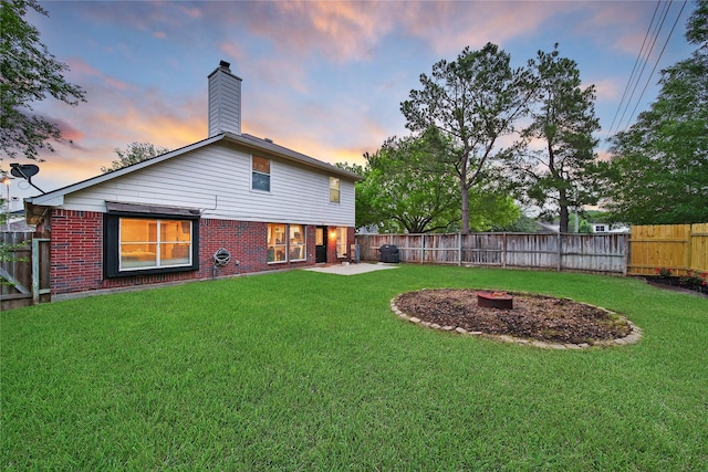 rear view of property featuring brick siding, a fenced backyard, an outdoor fire pit, and a yard