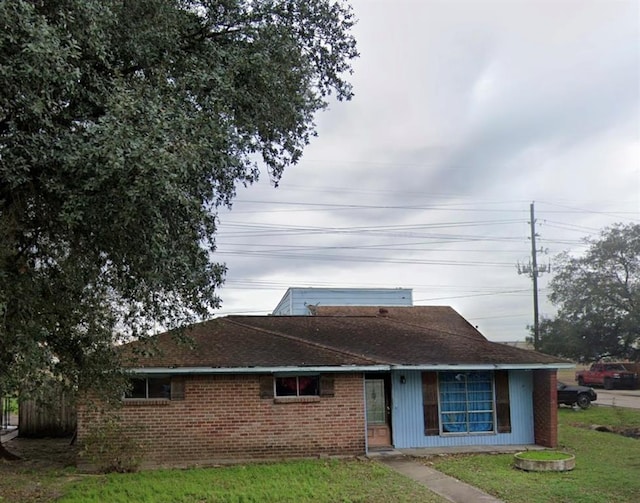single story home with brick siding, a shingled roof, and a front yard