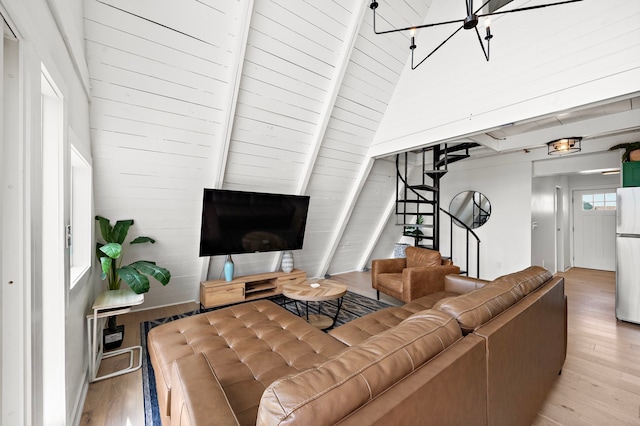 living room featuring beam ceiling, a notable chandelier, light wood-style flooring, and stairway