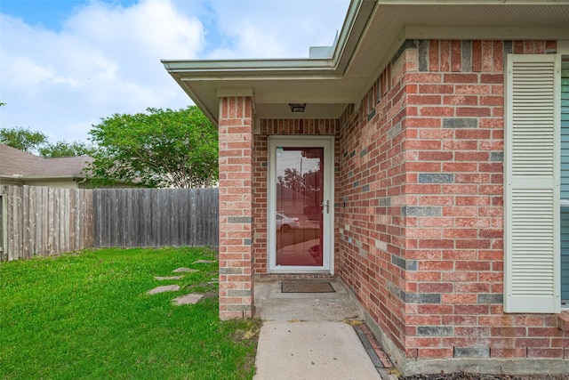 doorway to property with brick siding, a lawn, and fence