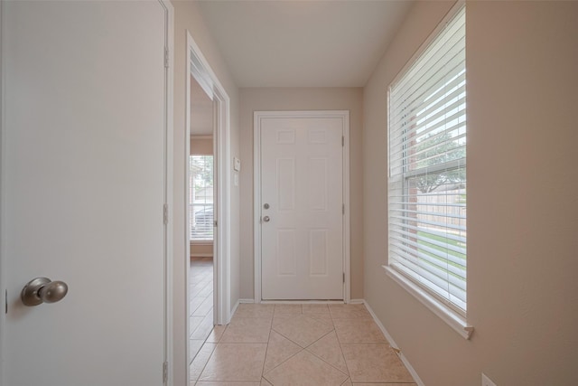 corridor featuring a healthy amount of sunlight, light tile patterned floors, and baseboards