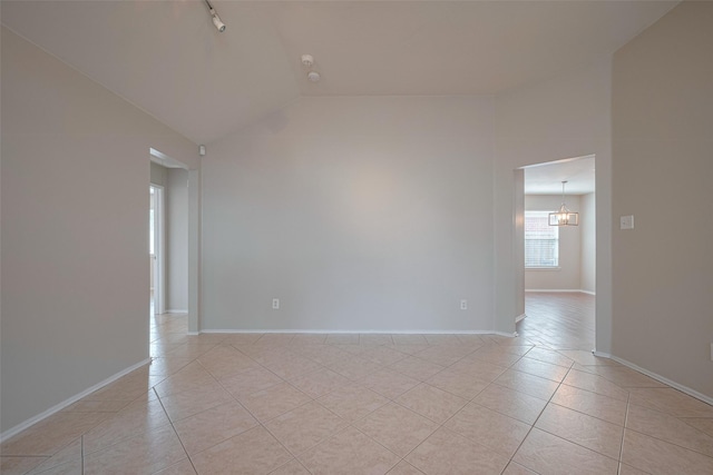 empty room featuring light tile patterned flooring, baseboards, a notable chandelier, and lofted ceiling
