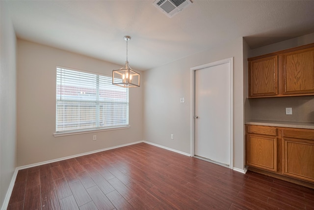 unfurnished dining area featuring baseboards, dark wood finished floors, a chandelier, and visible vents
