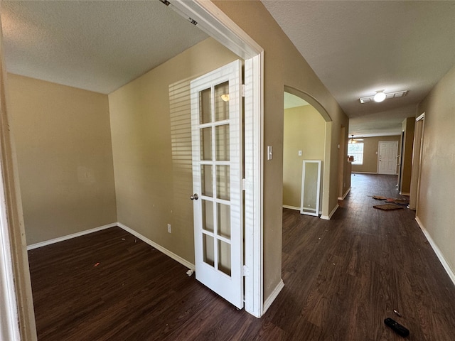 hall with arched walkways, a textured ceiling, baseboards, and dark wood-type flooring