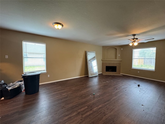 unfurnished living room featuring dark wood-style flooring, ceiling fan, a tiled fireplace, baseboards, and visible vents