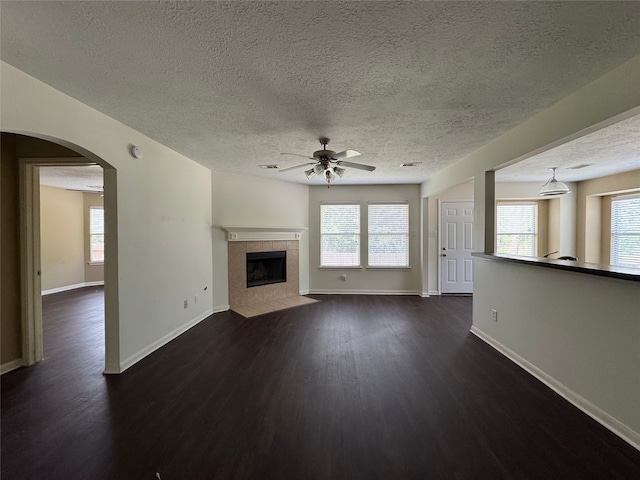 unfurnished living room featuring a ceiling fan, a textured ceiling, a wealth of natural light, and dark wood-type flooring