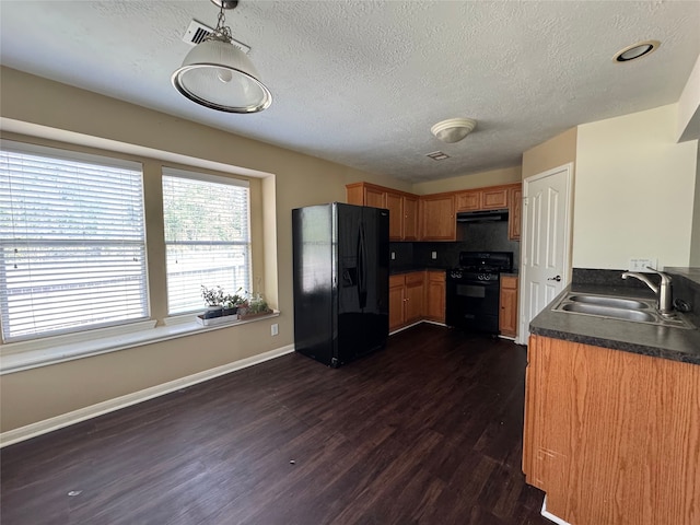 kitchen with dark countertops, dark wood-type flooring, under cabinet range hood, a sink, and black appliances