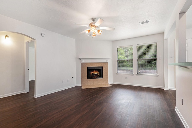900 Summer Wood Blvd, Conroe, TX 77303 - unfurnished living room with a ceiling fan, dark wood-style floors, arched walkways, a tiled fireplace, and a textured ceiling