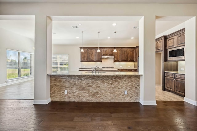 25034 Jennifer Heights Ct, Spring, TX 77389 - kitchen featuring wood finished floors, a sink, light stone counters, stainless steel microwave, and under cabinet range hood