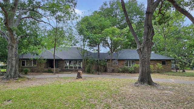 ranch-style house with curved driveway, roof with shingles, and a front lawn