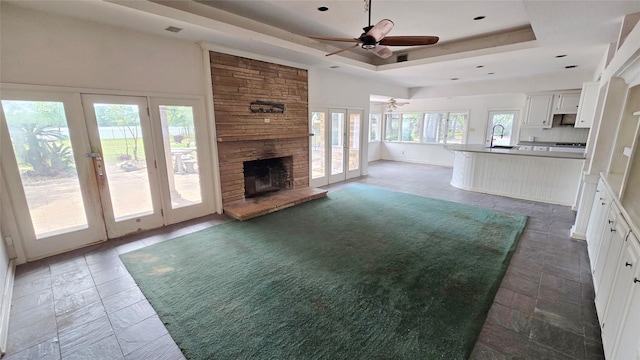 unfurnished living room featuring ceiling fan, a sink, a raised ceiling, a fireplace, and french doors