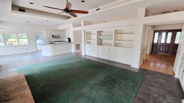 unfurnished living room with visible vents, a raised ceiling, built in shelves, dark tile patterned flooring, and a ceiling fan