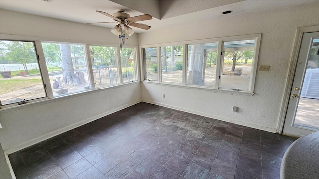 unfurnished sunroom featuring baseboards, stone finish floor, a textured wall, and a healthy amount of sunlight