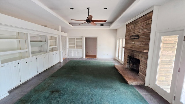 unfurnished living room with ceiling fan, built in shelves, a tray ceiling, and a fireplace
