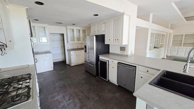 kitchen featuring appliances with stainless steel finishes, a sink, light countertops, white cabinets, and glass insert cabinets