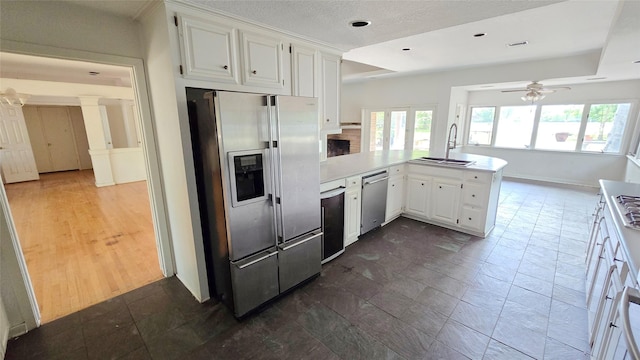 kitchen with a sink, a peninsula, white cabinets, a ceiling fan, and stainless steel appliances