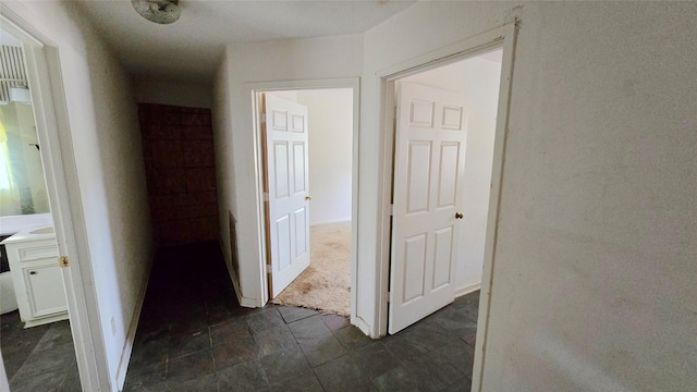 hallway with baseboards and dark colored carpet