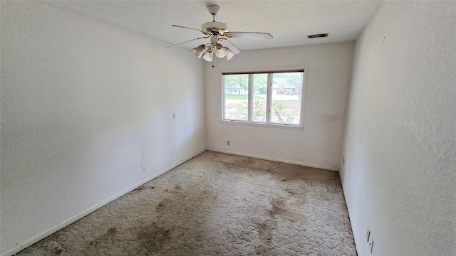 empty room featuring a ceiling fan, visible vents, baseboards, a textured wall, and carpet