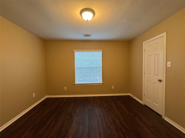spare room featuring visible vents, dark wood finished floors, and baseboards