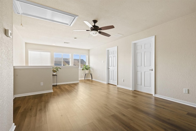 empty room featuring a ceiling fan, attic access, visible vents, wood finished floors, and baseboards